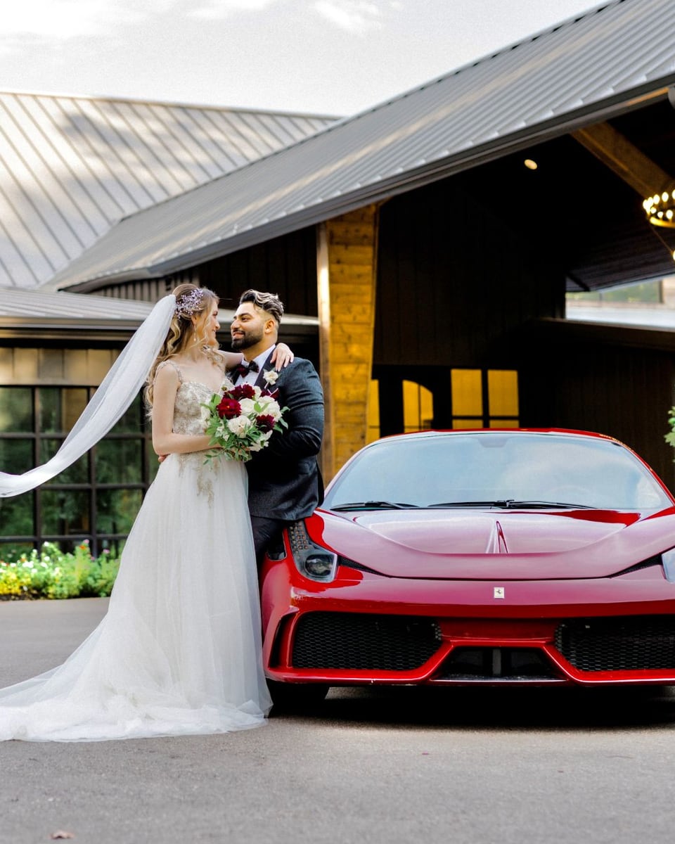 Bride and groom beside a red Ferrari outside their wedding venue